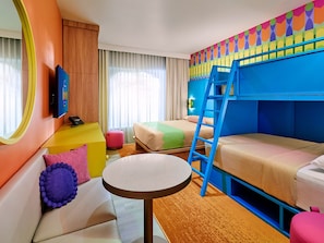 Hotellihuone, jossa on kerrossänky, sohva, pieni pyöreä pöytä, televisio ja ikkuna, jossa on verhot.