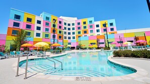 A colorful hotel with a swimming pool, outdoor seating, and a clear blue sky. - Universal Kids Resort Hotel (Frisco)