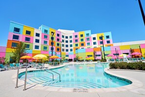 A colorful hotel with a swimming pool, outdoor seating, and a clear blue sky. - Universal Kids Resort Hotel (Frisco)