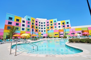 Un hotel colorido con piscina, asientos al aire libre y un cielo azul brillante.