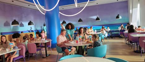 A restaurant with round tables and chairs, people dining, and a blue and purple color scheme.