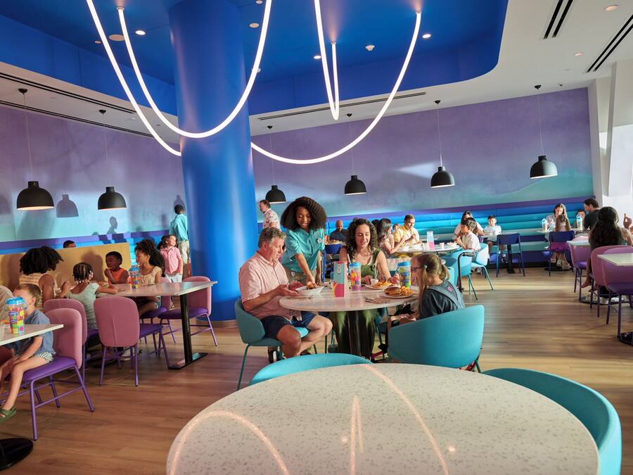 A restaurant with round tables and chairs, people dining, and a blue and purple color scheme.