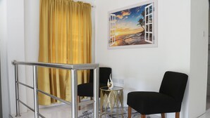 A room with a black chair, a round table with a decorative item, a yellow curtain, and a framed picture of a beach scene. - Cozy 1-bedroom apartment in beautiful Laborie with AC (Laborie)