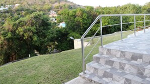A staircase with metal railings leading to a grassy area with a view of a hill and buildings. - Cozy 1-bedroom apartment in beautiful Laborie with AC (Laborie)