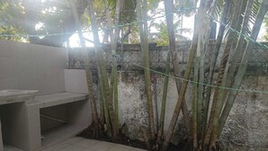 A tiled patio area with a concrete bench, bamboo plants, and a chain-link fence. - Spacious, centrally located residence with a private pool! Perfect for Families! (Cancún)
