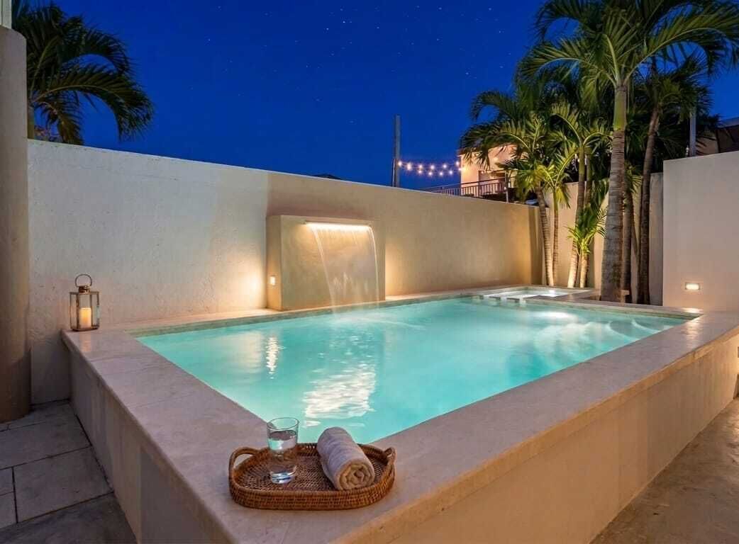 A rectangular pool with a waterfall feature, surrounded by palm trees and a night sky.