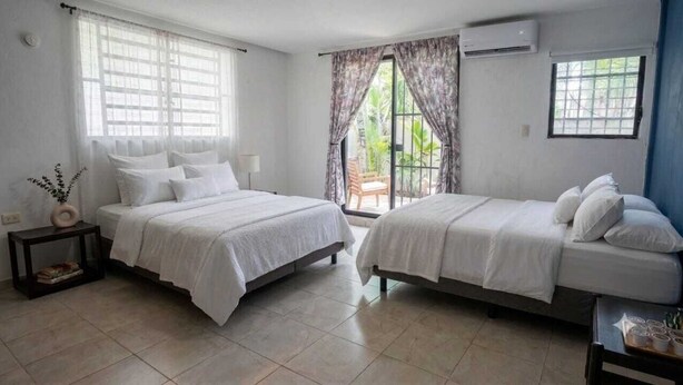 A hotel room with two beds, a small table, and a window with curtains. - Spacious, centrally located residence with a private pool! Perfect for Families! (Cancún)