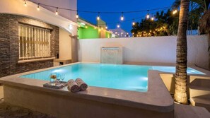 A swimming pool with a waterfall feature, surrounded by a white wall and a palm tree. - Family home in a safe neighborhood with spacious bedrooms and a private pool (Cancún)
