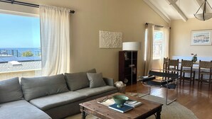 Ein Wohnzimmer mit einer Couch, einem Couchtisch, einem Bücherregal und Blick auf das Meer.