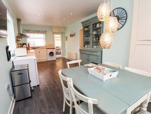 A kitchen with a washing machine, a dining table with chairs, and a clock on the wall. - Gelli - Morfa Nefyn (Pwllheli)