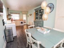 A kitchen with a washing machine, a dining table with chairs, and a clock on the wall.