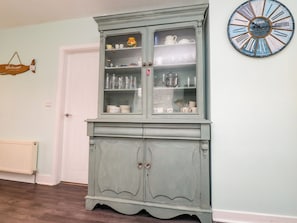 Ein Zimmer mit hellblauer Wand, einer weißen Tür, einem Schrank mit Glastüren und einer Wanduhr.