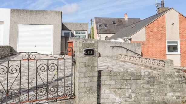 A gated entrance with a sign, a garage door, and a brick building. - Gelli - Morfa Nefyn (Pwllheli)