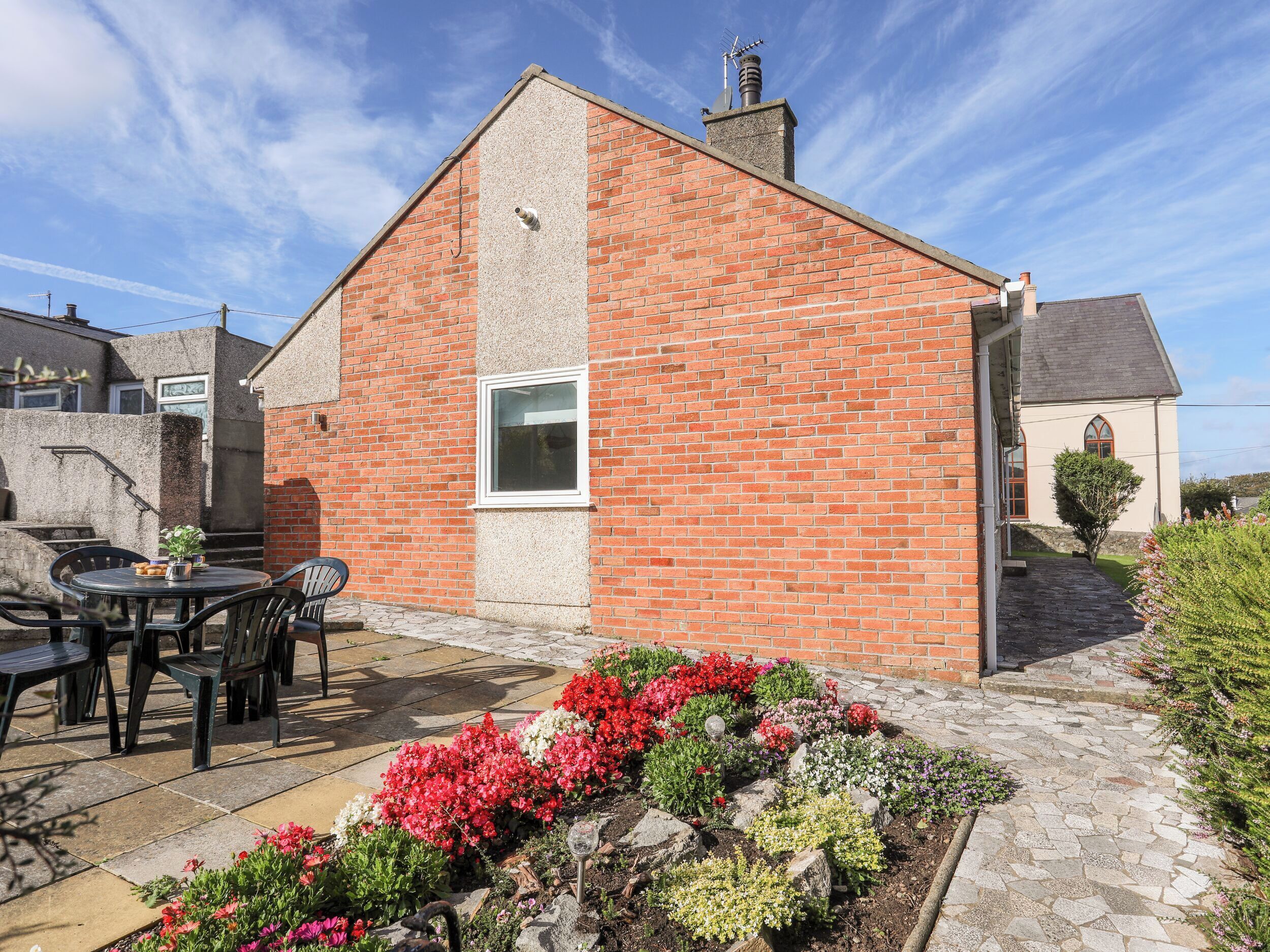 A brick building with a window, outdoor seating, and a flower bed.