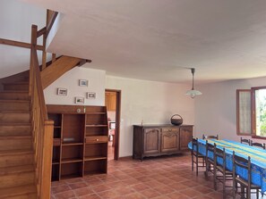 Una escalera de madera conduce a un comedor con suelo de baldosas, un armario de madera y una mesa con sillas.