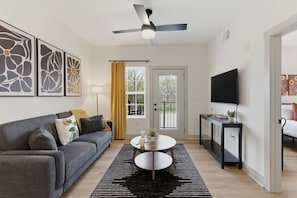 A modern living room with a grey sofa, a round coffee table, a ceiling fan, and a TV on a stand.