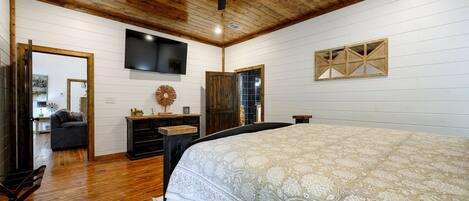 Un dormitorio con una cama grande, techo de madera, ventilador de techo, televisor montado en la pared y un armario de madera.