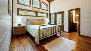 A bedroom with a bed, nightstand, and a window with a view of trees. - The Retreat at Red Fern - Excellent Location (Broken Bow)