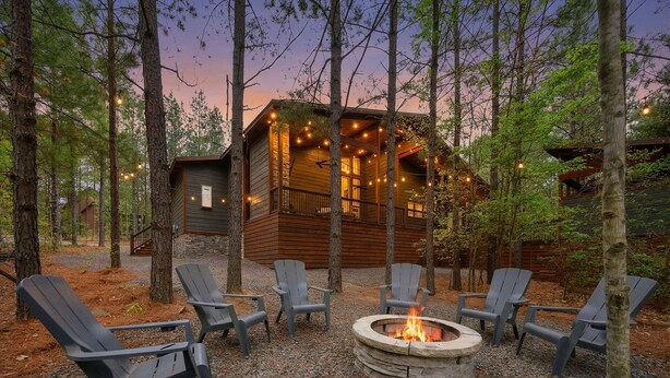 A cabin with a stone fire pit surrounded by Adirondack chairs, set in a forest. - The Retreat at Red Fern - Excellent Location (Broken Bow)