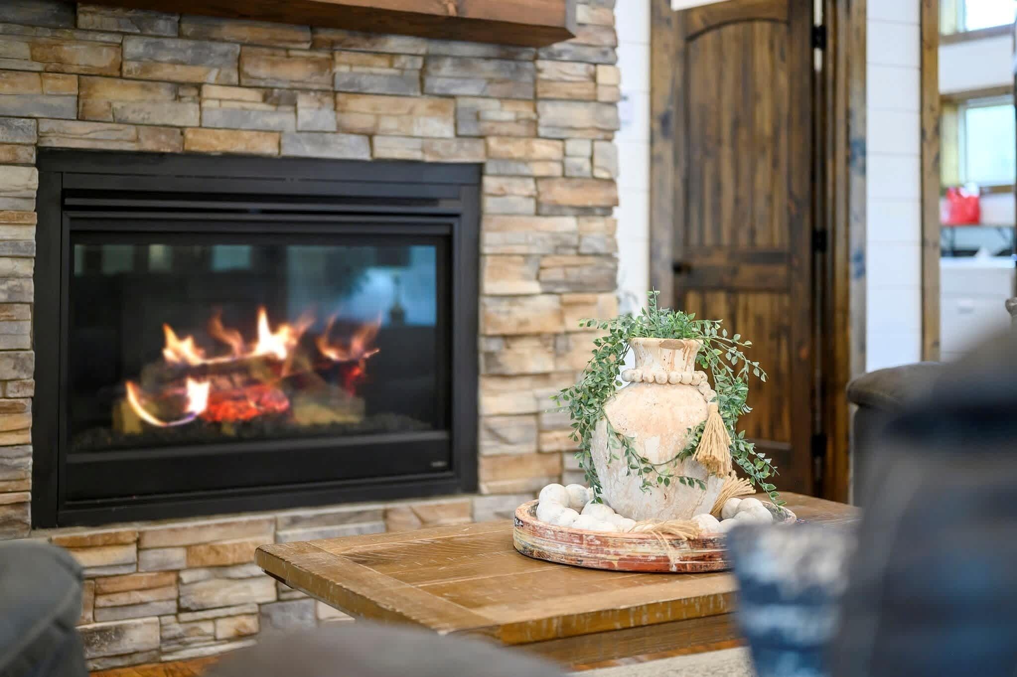 Una chimenea con pared de piedra, una mesa de madera con un objeto decorativo y un sofá en una sala de estar.