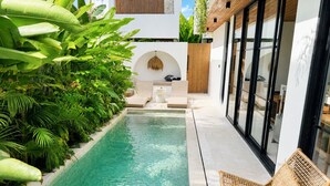 A modern pool area with a clear pool, surrounded by lush greenery and a wicker lounge chair. - 2BR Private Pool Villa • Near Cemagi Beach & Canggu (Badung)