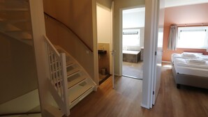 A hotel room with a wooden staircase, a bed with white linens, and a bathroom with a sink and mirror. - New, Luxury Holiday Home in the Heart of Friesland (Leons)