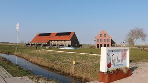A building with a red roof, a signboard, and a water channel. - New, Luxury Holiday Home in the Heart of Friesland (Leons)