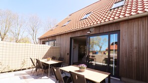 An outdoor patio with tables and chairs, a wooden fence, and a building with a tiled roof and large windows. - New, Luxury Holiday Home in the Heart of Friesland (Leons)