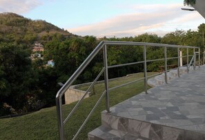 Eine Treppe mit Metallgeländern führt zu einer Terrasse mit Blick auf eine Hügellandschaft und Gebäude.