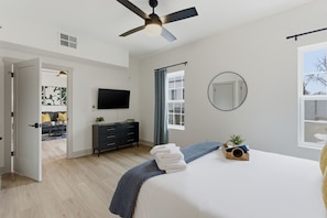 A bedroom with a bed, a ceiling fan, a TV, a dresser, a window, and a door leading to another room. - Boutique Loft w/ Patio, Rooftop Views + In-Unit W/D (Murfreesboro)