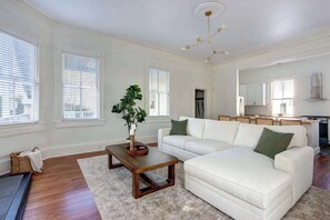 Een woonkamer met een witte bank, een houten salontafel en een groot raam met jaloezieën.