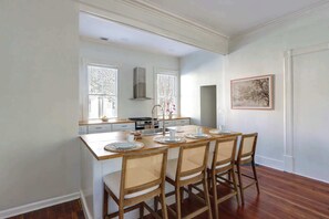 Een keuken met een centraal eiland, witte kasten en een eethoek met vier stoelen.