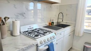 Une cuisine équipée d’une cuisinière à gaz, d’un évier, d’un dosseret en marbre et de meubles blancs.