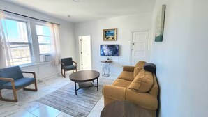 Un salon comprenant un canapé, un fauteuil, une table basse, un téléviseur et des œuvres d’art accrochées au mur.