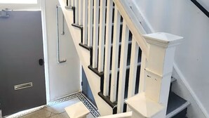 Un escalier avec des rampes et une main courante blanches, menant à l’étage supérieur.