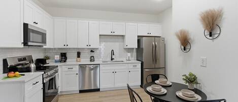 A modern kitchen with white cabinets, stainless steel appliances, a dishwasher, and a dining area with a table and chairs.