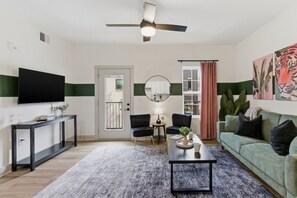 Ein modernes Wohnzimmer mit Flachbildfernseher, Deckenventilator, Sofa, Couchtisch und einem Essbereich mit Tisch und Stühlen.