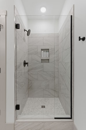 Una cabina doccia con pareti in vetro, pavimento in marmo e un piccolo ripiano con articoli da toilette.