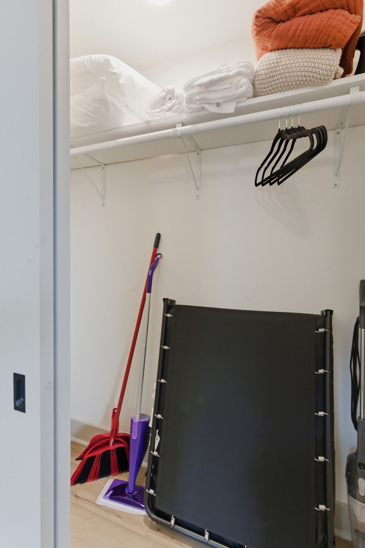 A room with a bed, a black mat on the floor, a vacuum cleaner, and a broom.