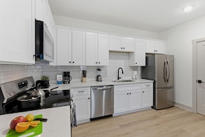 A modern kitchen with white cabinets, stainless steel appliances, and a wooden floor. - Boutique Loft w/ Patio, Rooftop Views + In-Unit W/D (Murfreesboro)
