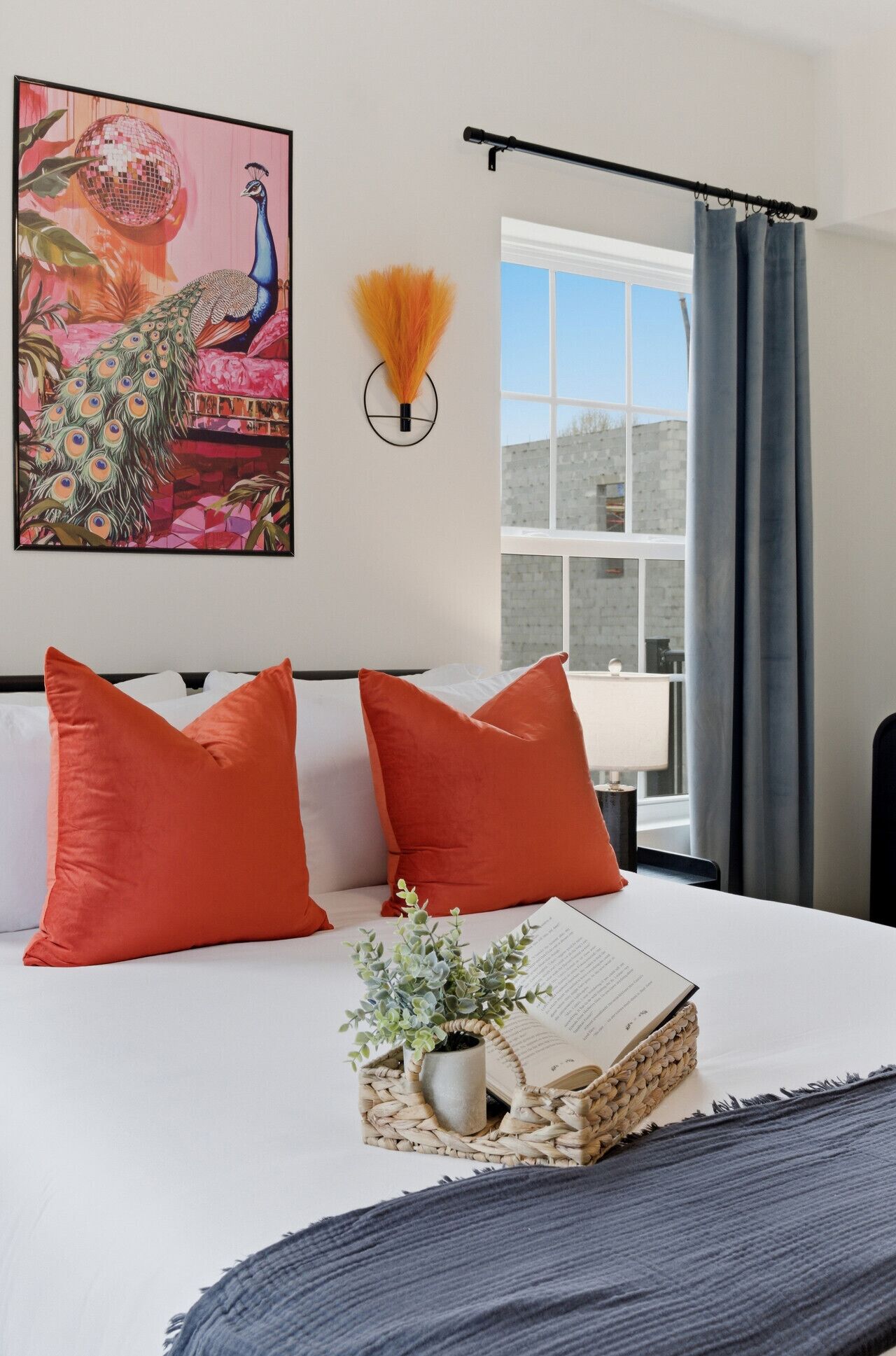 Ein Bett mit zwei orangefarbenen Kissen, einem kleinen Topfpflanzen und einem gerahmten Bild an der Wand.