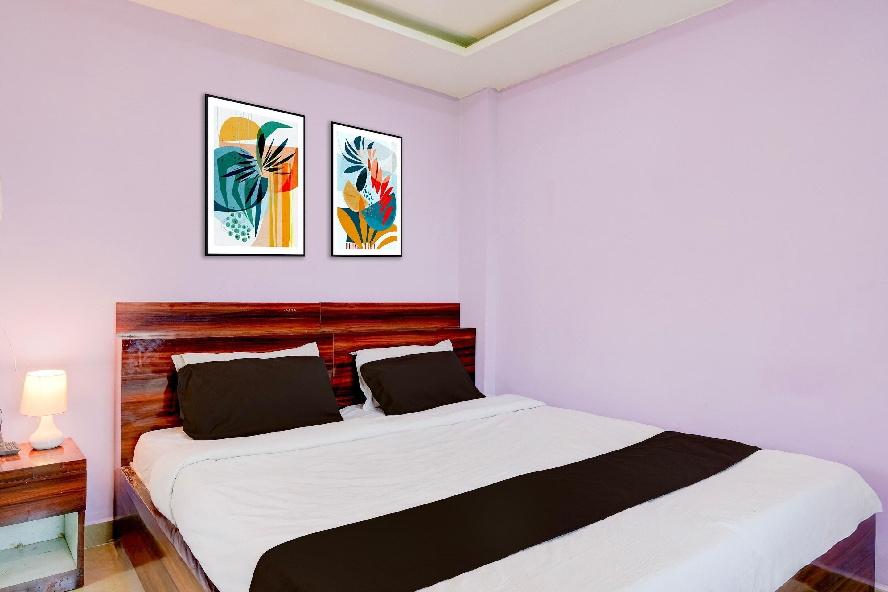 Una cama bien hecha con cabecera de madera, una lámpara de noche y dos cuadros abstractos en la pared.