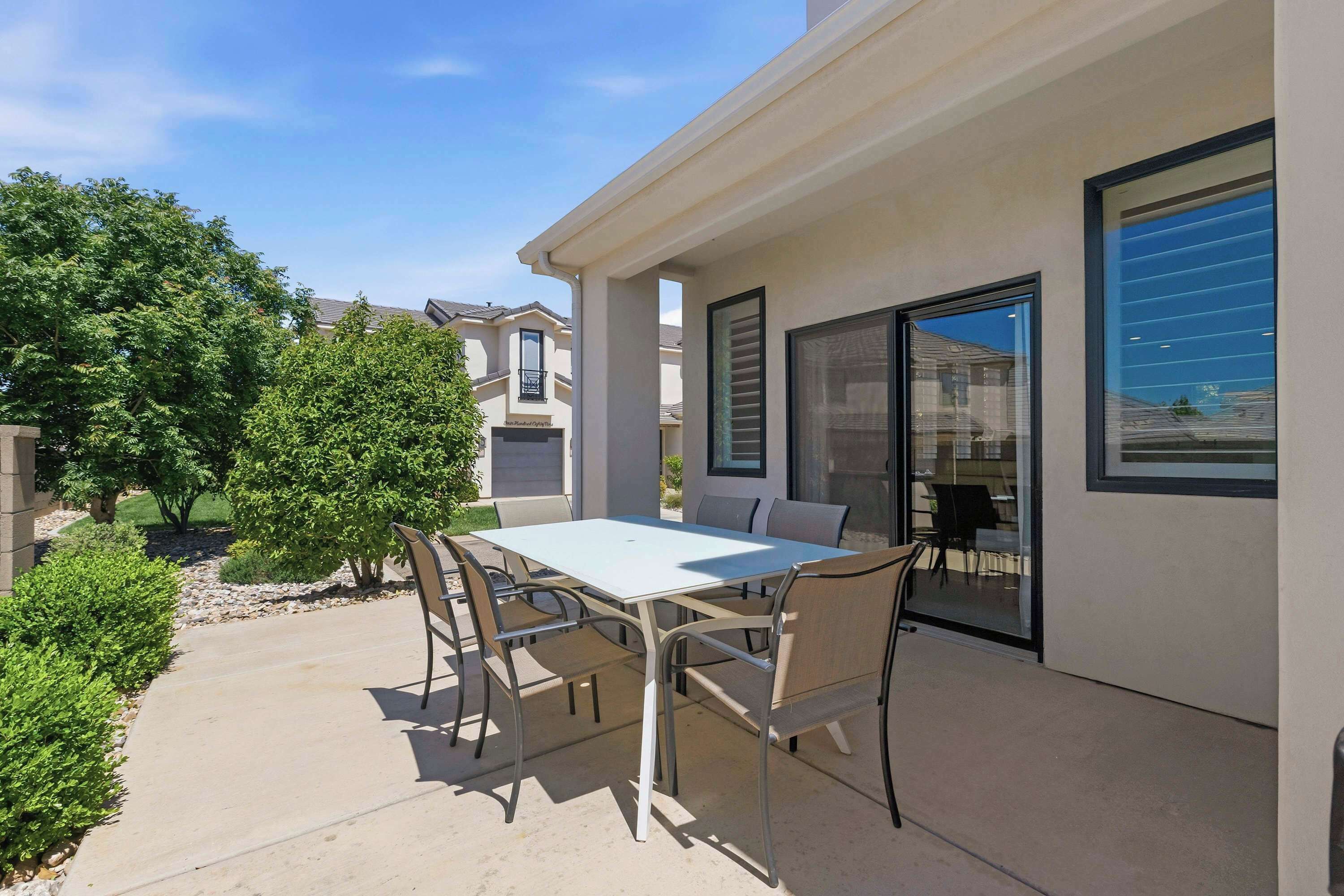 Une terrasse extérieure avec une table et des chaises, une porte vitrée et une vue sur les maisons voisines.