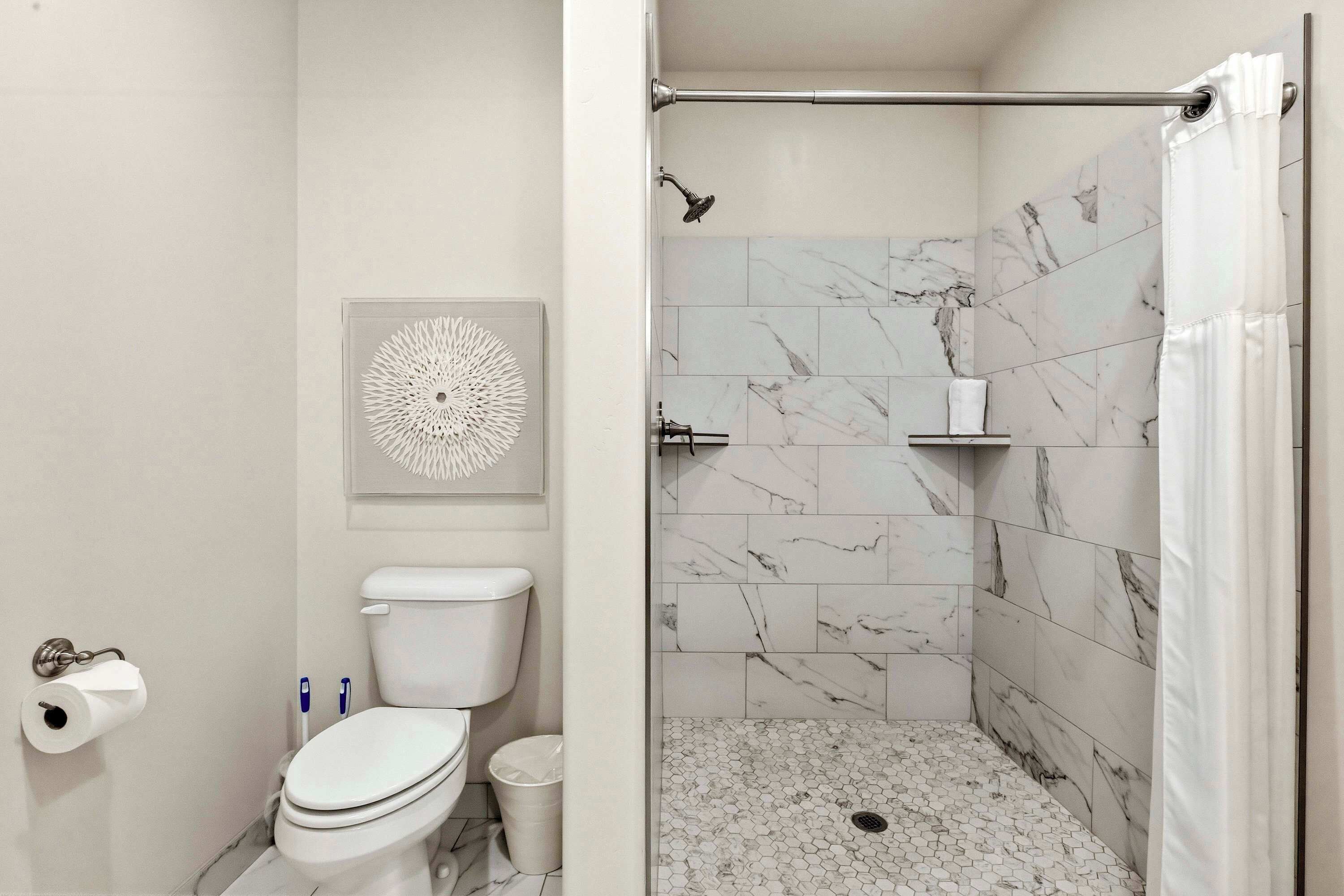 Une salle de bain comprenant des toilettes, un lavabo, une douche avec un mur en marbre et un porte-rouleau de papier toilette.