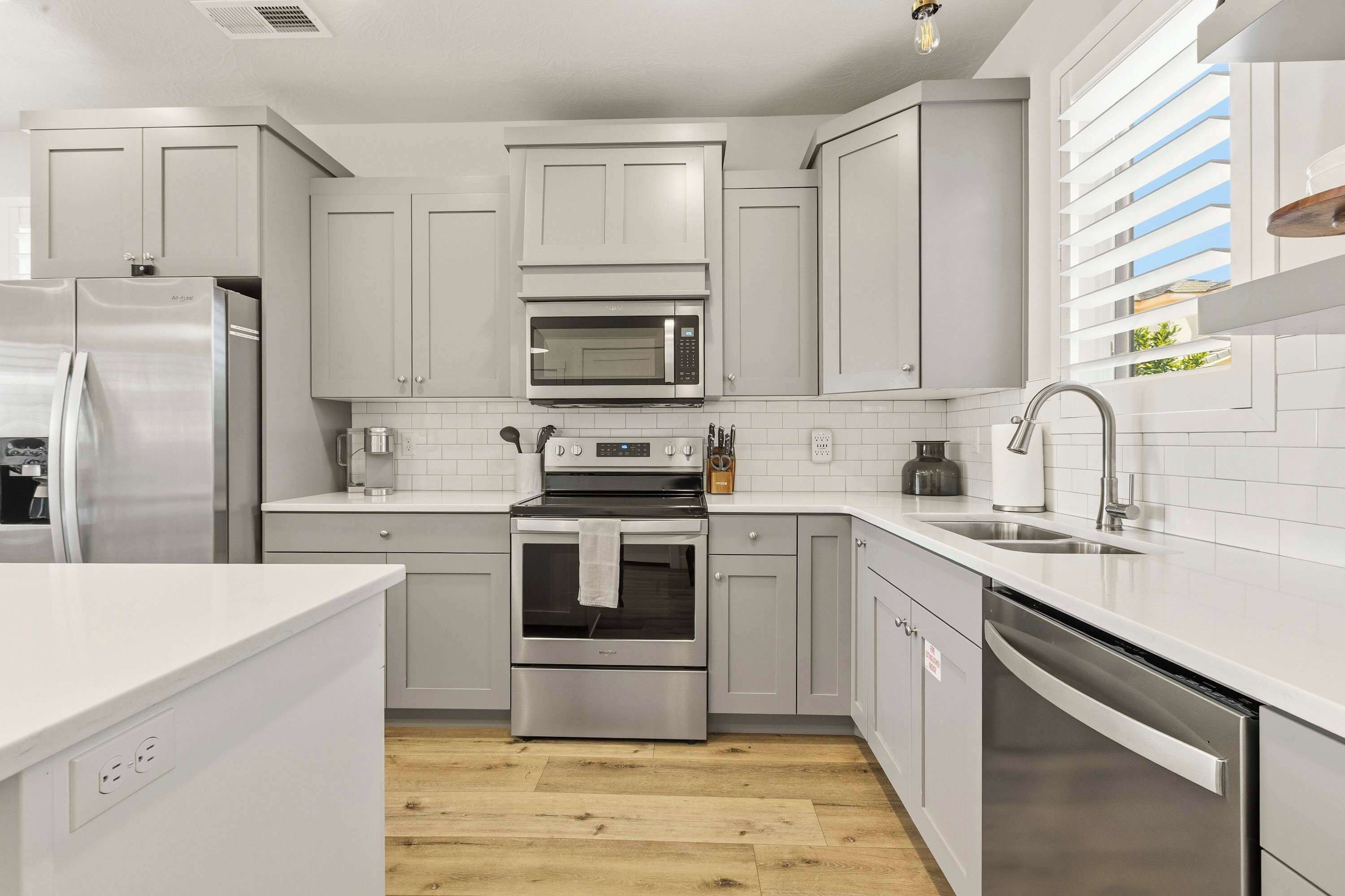 Una cocina moderna con electrodomésticos de acero inoxidable, armarios blancos y piso de madera.