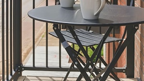 Un patio con mesa y sillas, una reja y un edificio de ladrillo al fondo.
