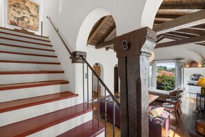 A staircase with wooden steps and a metal handrail, leading to a room with a sofa, chairs, and a view of the outdoors.