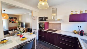 Eine moderne Küche mit Mikrowelle, Backofen und Spüle. Ein Esstisch mit Stühlen und ein Fernseher im Hintergrund sind ebenfalls vorhanden.