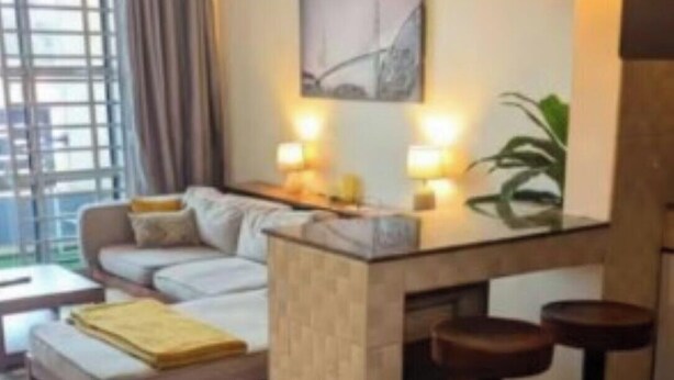 Ein modernes Wohnzimmer mit einer Couch, einem Couchtisch, einer Bar mit Hockern, Pendelleuchten und einem großen Fenster mit Vorhängen.