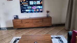 Ein Wohnzimmer mit einem an der Wand befestigten Flachbildfernseher, einem Holzschrank darunter und einem Couchtisch im Vordergrund.